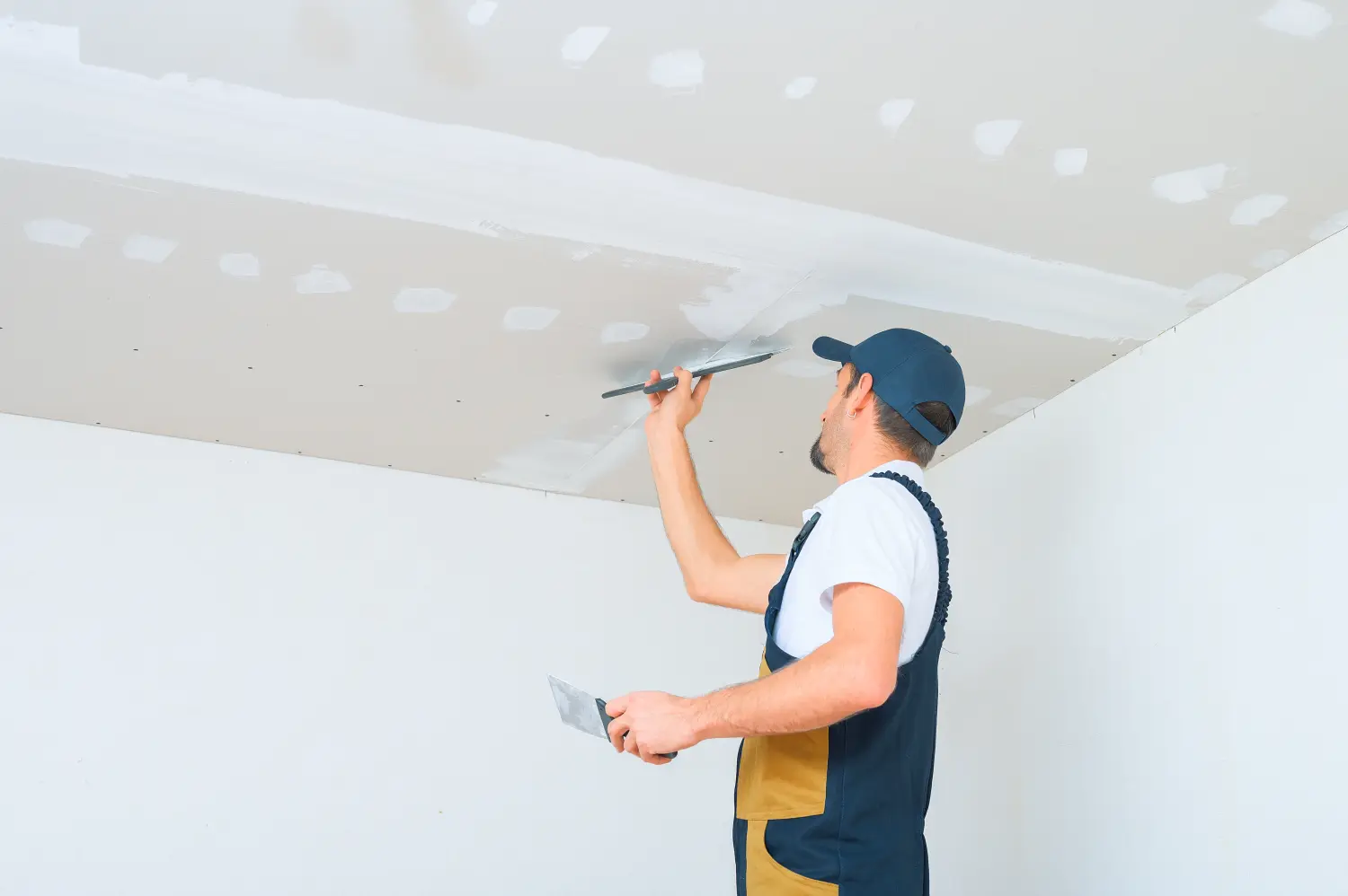 Ein uniformierter Arbeiter trägt Spachtelmasse auf die Gipskartondecke auf. Spachtelmasse auf die Fugen der Gipskartonplatten.