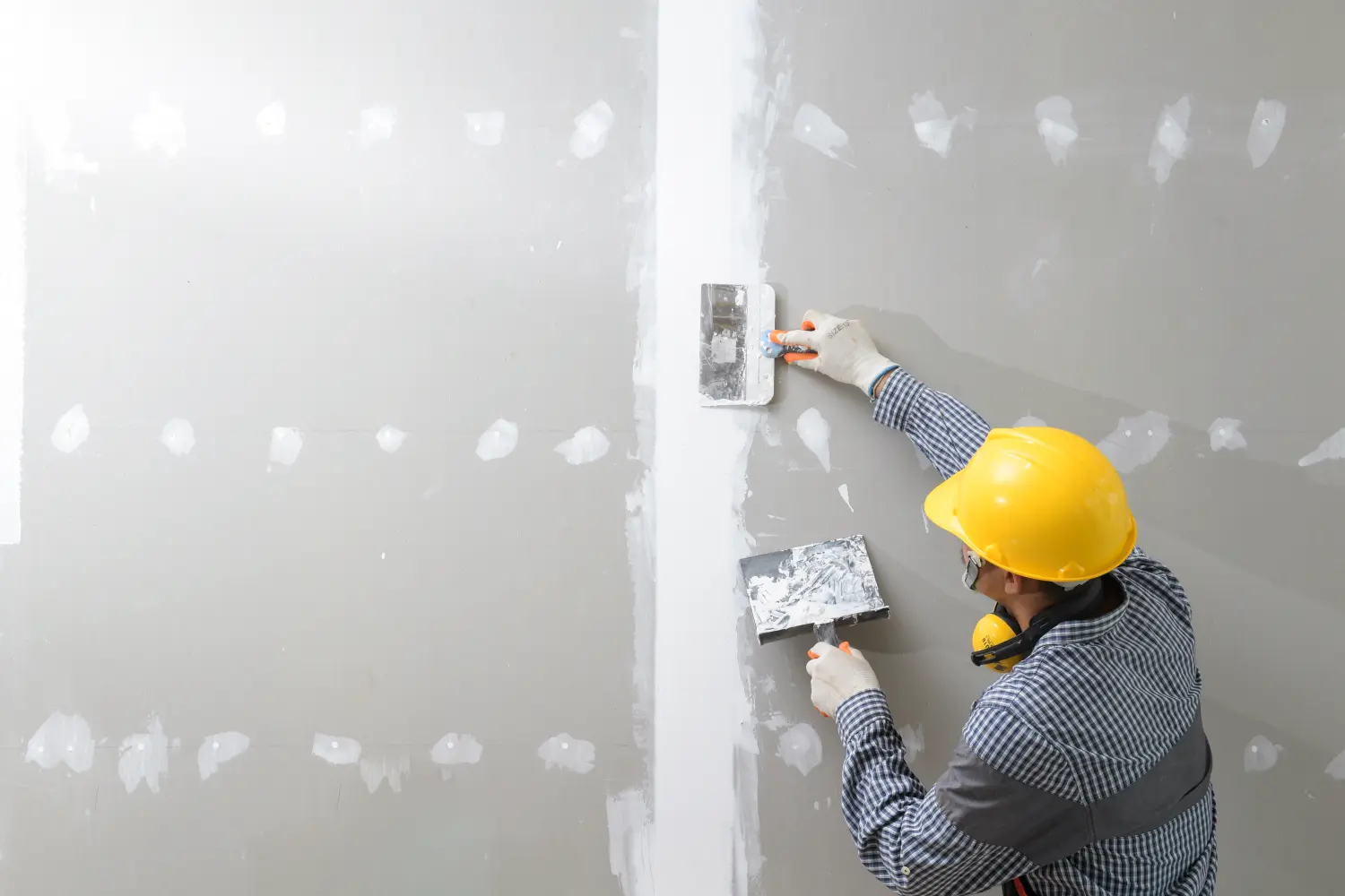 Innendekoration, Bau, Möbel, Einbau. Gipser in Arbeitsuniform verputzt die Wand im Innenbereich.
